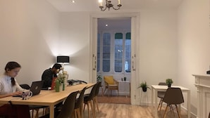 A dining area with a wooden table, chairs, and a chandelier. There are two people seated at the table, one using a laptop. - Sweet BCN Youth Hostel (Barcelona)