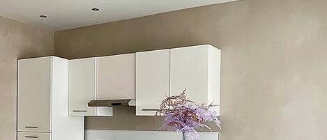 A modern kitchen with white cabinets, a dining table set for two, and a vase with purple flowers.