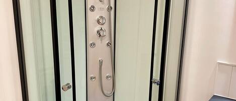 A glass-enclosed shower stall with a handheld showerhead, a built-in seat, and a drain.