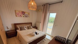 Ein Schlafzimmer mit Bett, Nachttischen, einer Lampe, einem Gemälde, einer Deckenleuchte, einem Fenster mit Vorhängen und Blick ins Freie.