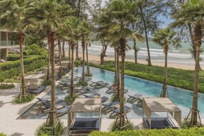 Un espace piscine doté de chaises longues, de palmiers et offrant une vue sur la plage.