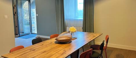 Comedor con mesa de madera, sillas rojas, un jarrón con flores y vista a un balcón a través de puertas de vidrio.