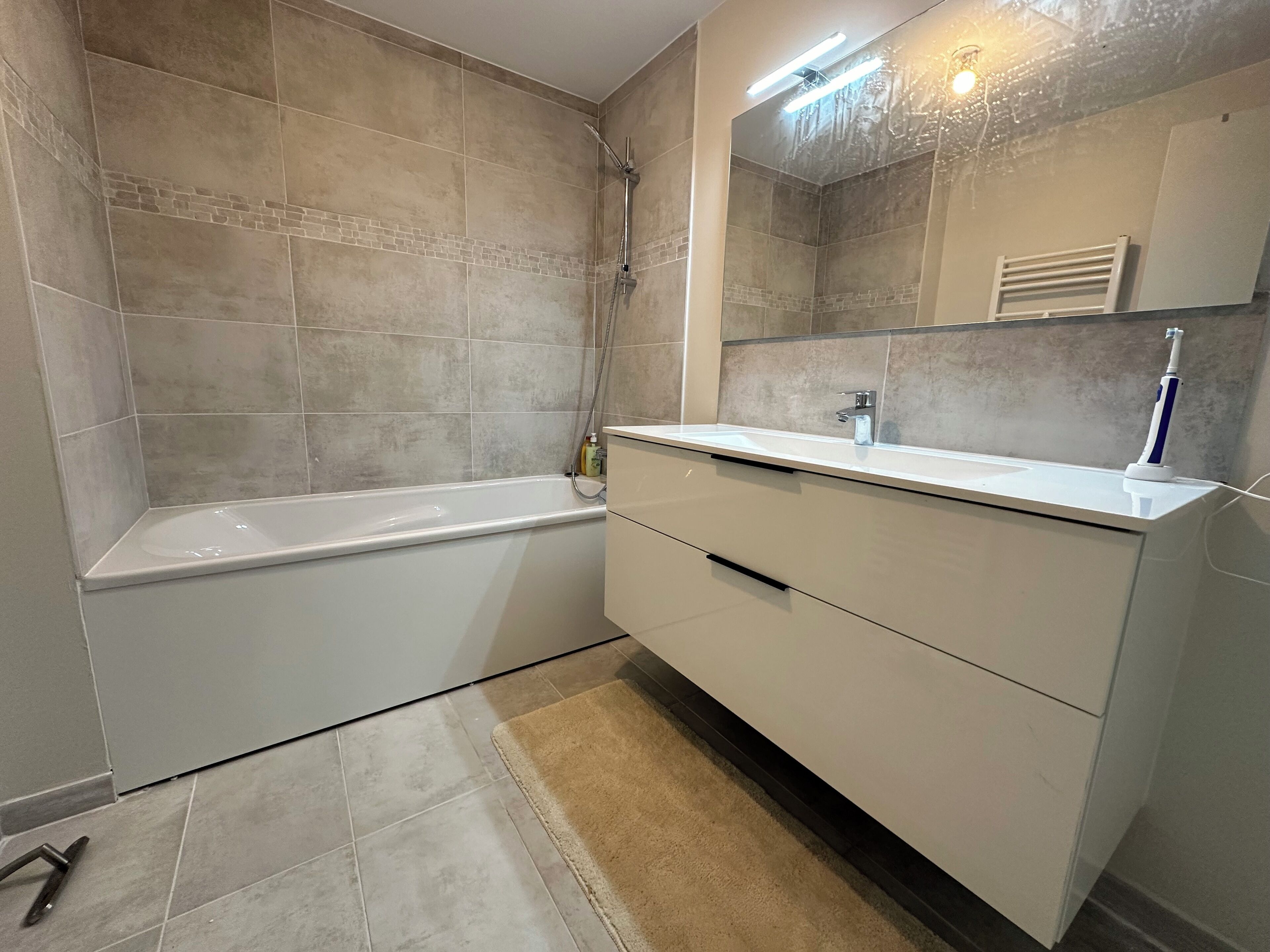 A modern bathroom with a bathtub, a vanity with a mirror, and a showerhead.