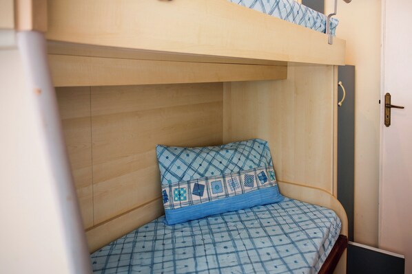 A bunk bed with a patterned mattress and pillow, wooden walls, and a door with a handle.