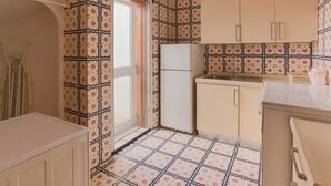 A compact kitchen with patterned wallpaper, a refrigerator, and basic cabinetry.