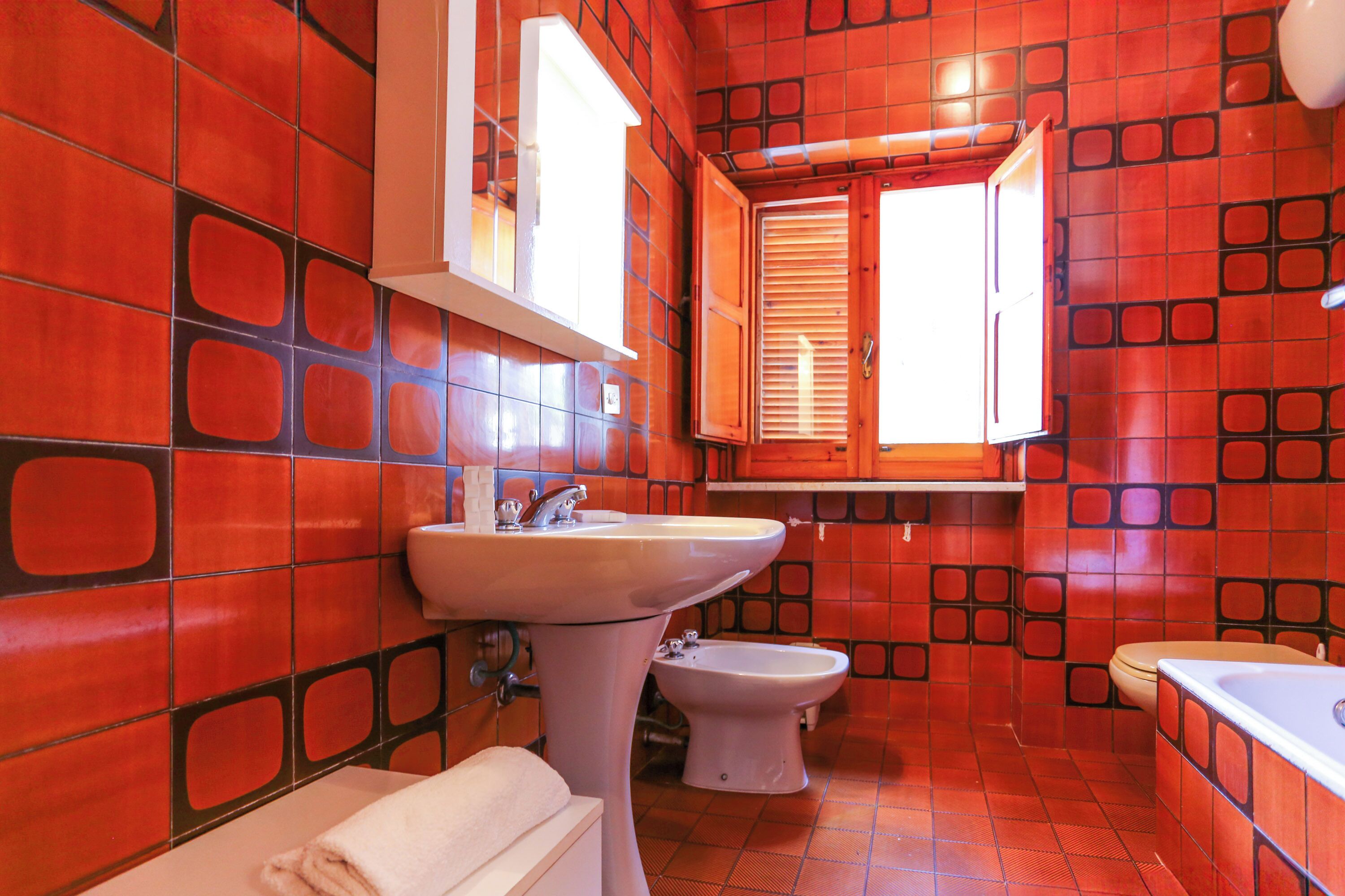 A bathroom with red tiled walls, a white sink, a bidet, and a bathtub.