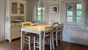 Comedor con mesa y sillas blancas, un armario blanco con puertas de vidrio y una ventana con cortinas.