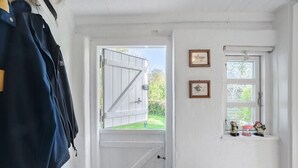 Una habitación con una puerta blanca, un ventanal con vistas y un perchero con una chaqueta azul.