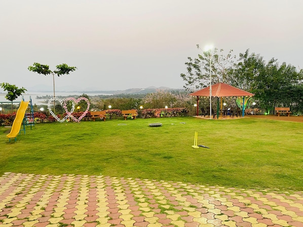 A park with a playground, a heart-shaped decoration, a gazebo, and a view of distant hills. - Kapildhara Agro Tourism Resort (Igatpuri)