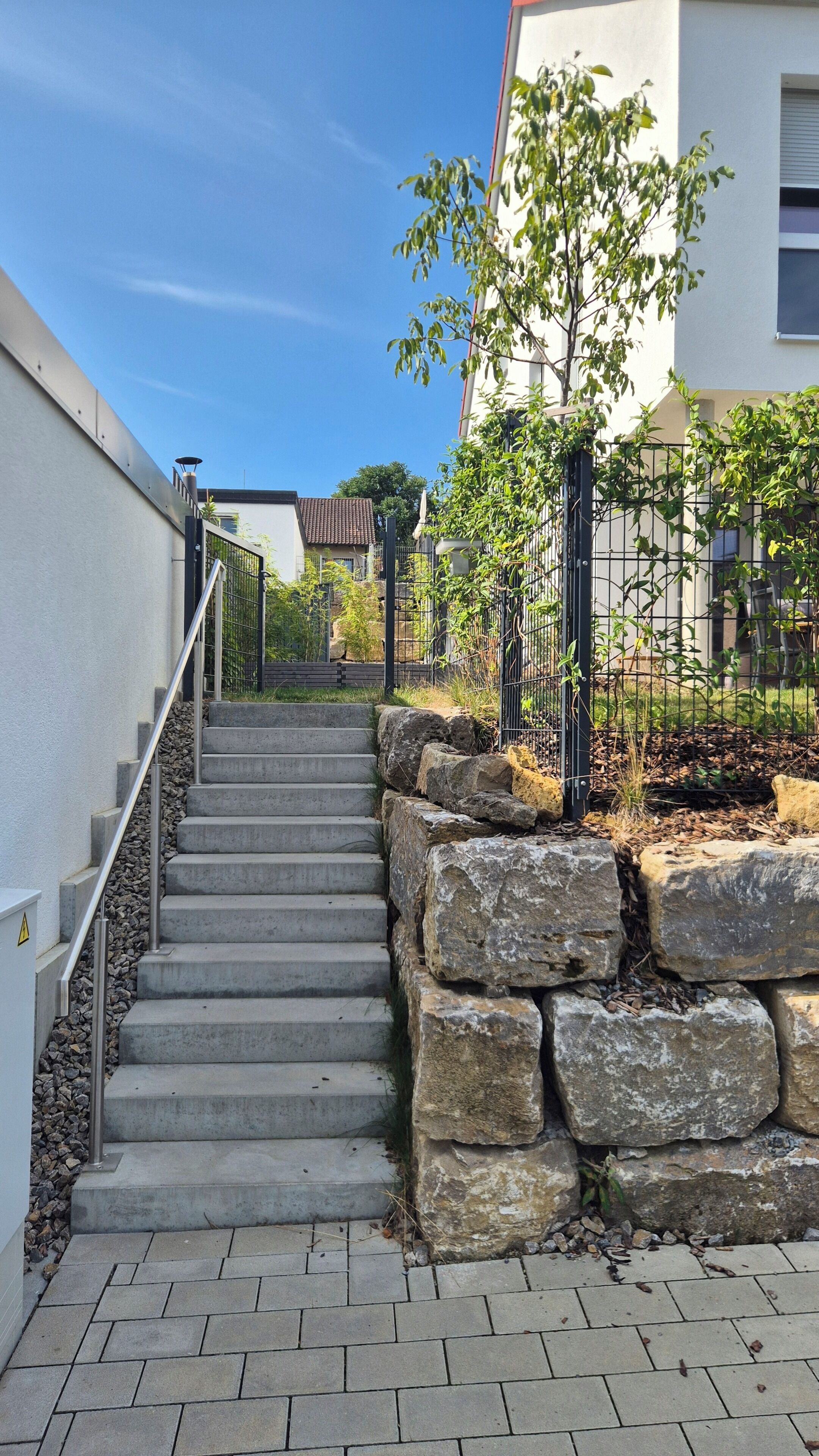 Una escalera conduce a un edificio de fachada blanca, con barandilla metálica y pared de piedra en la base.