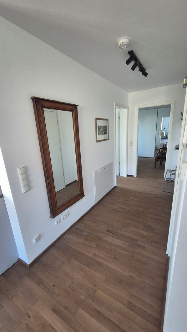 Amplia habitación con piso de madera, un espejo grande, un cuadro enmarcado y una lámpara en el techo.