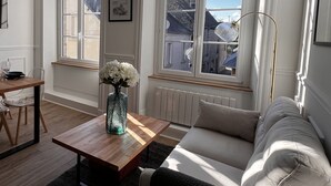 A modern living room with a wooden coffee table, a white sofa, and a view of the city through large windows. - House for 10 people in the center of Sainte Mère Eglise (Sainte-Mère-Église)
