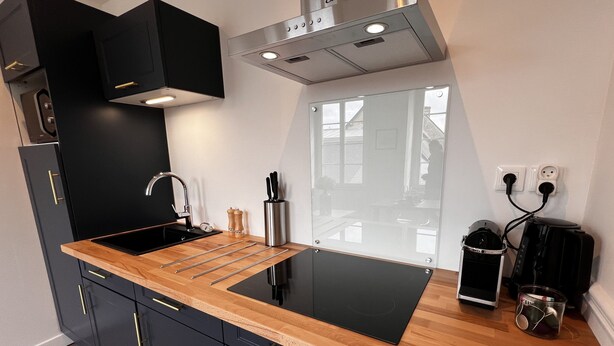 A modern kitchen with a black countertop, stainless steel sink, and a window overlooking a residential area. - House for 10 people in the center of Sainte Mère Eglise (Sainte-Mère-Église)