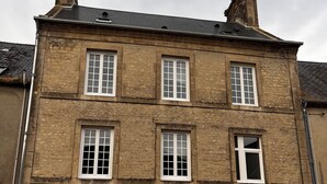 A two-story stone building with six windows, a central door, and a small light fixture above the door. - House for 10 people in the center of Sainte Mère Eglise (Sainte-Mère-Église)