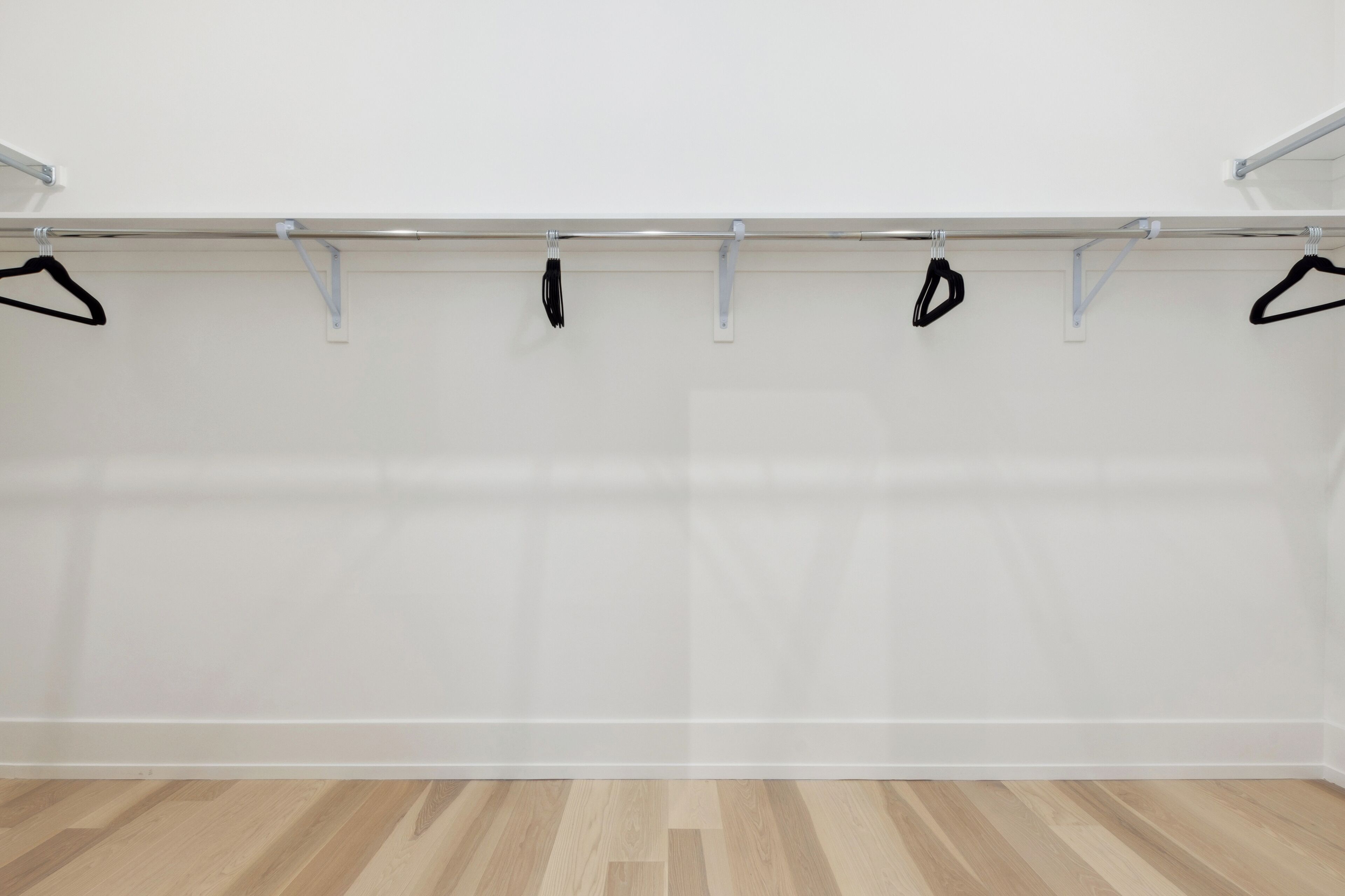 Een kamer met een houten vloer en een kledingrek met zwarte hangers.