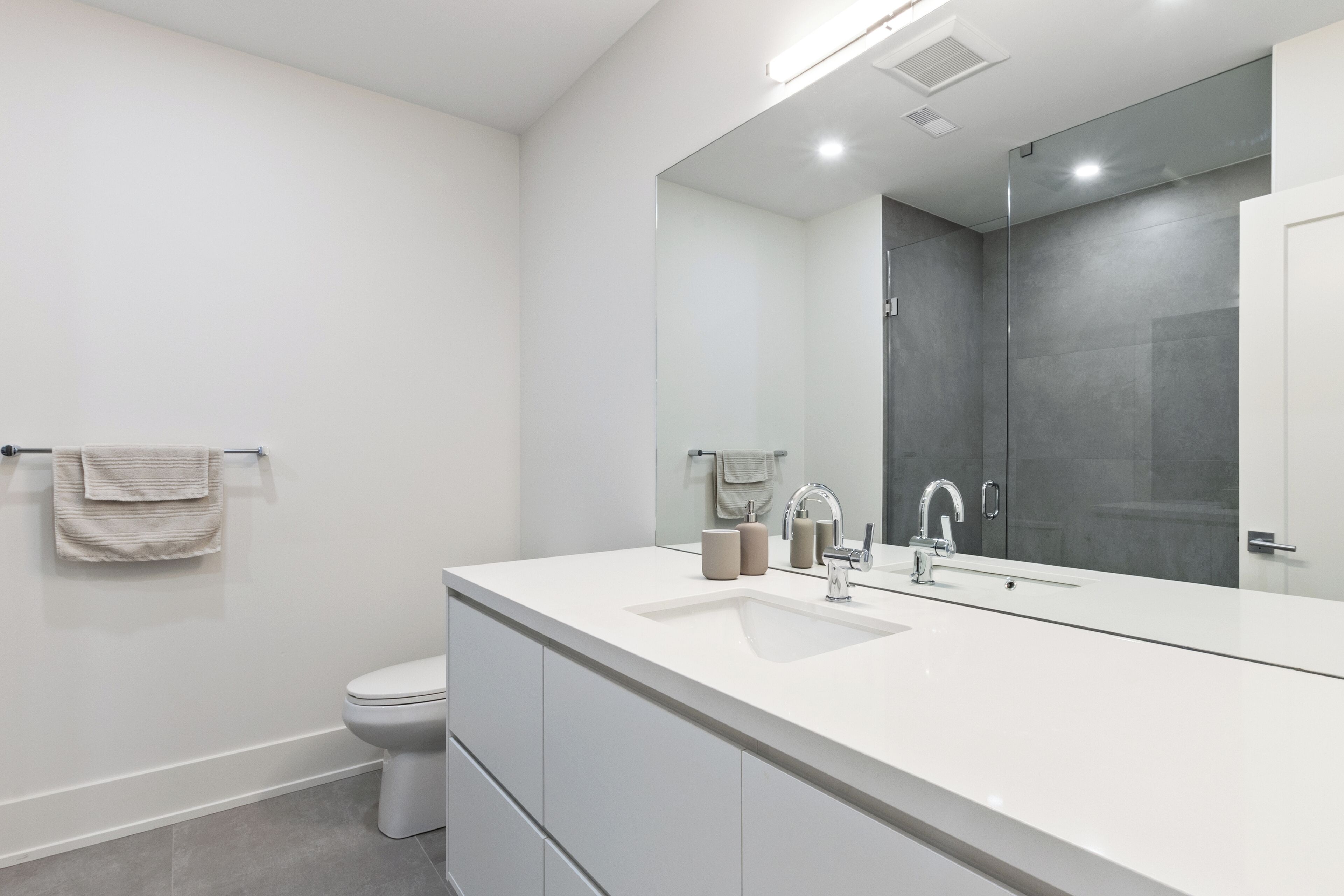 Un baño moderno con lavamanos, espejo e inodoro blancos.