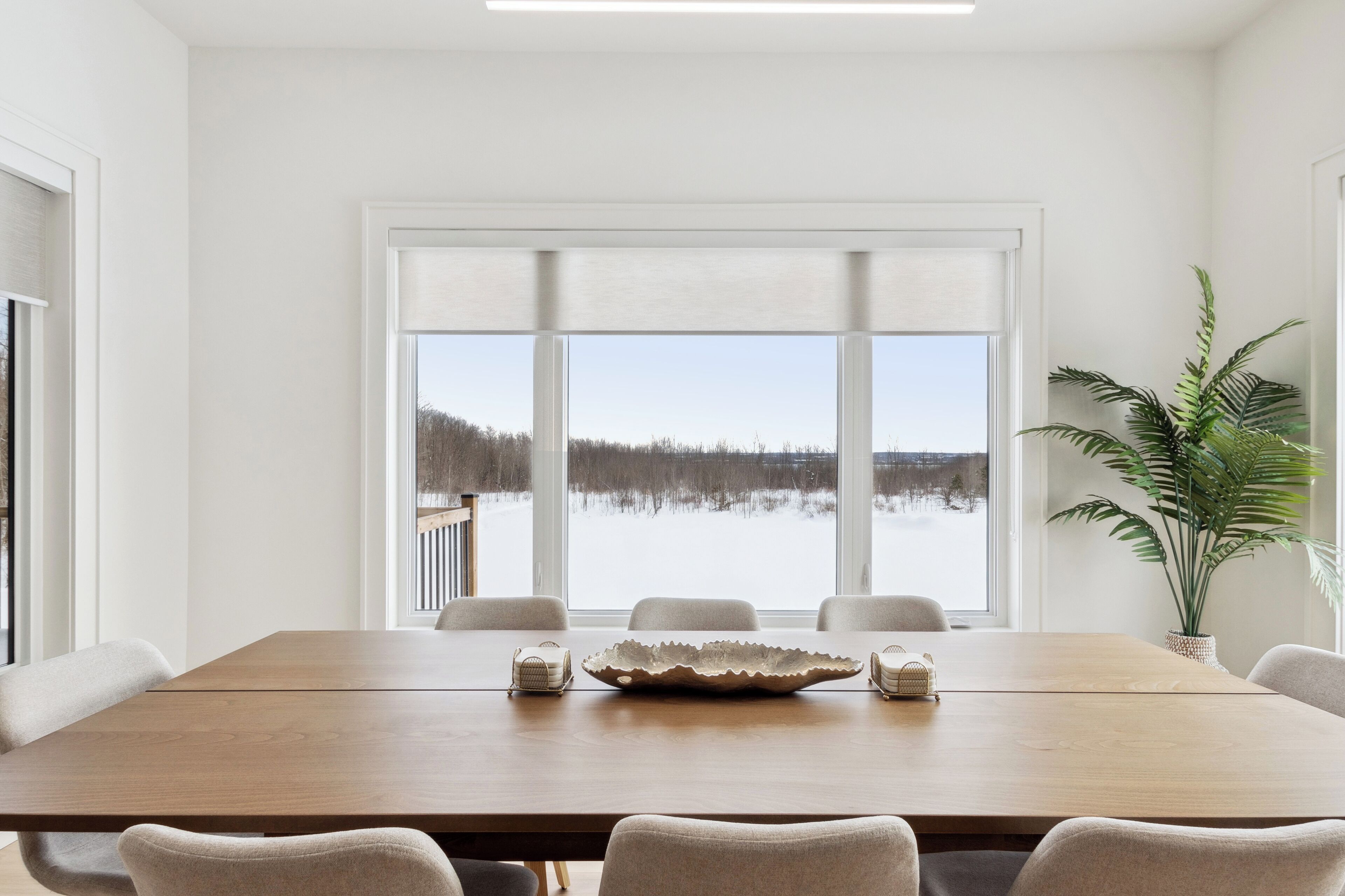 A dining area with a large table, chairs, and a view of a snowy landscape through large windows.