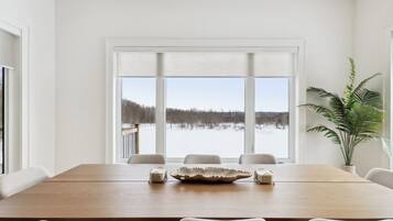 A dining area with a large table, chairs, and a view of a snowy landscape through large windows.