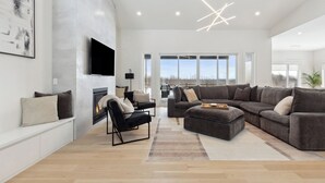 Un amplio salón con chimenea, un sofá modular grande y un televisor de pantalla plana montado en la pared.