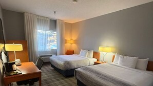 A hotel room with two beds, a desk, a chair, and a window with curtains.
