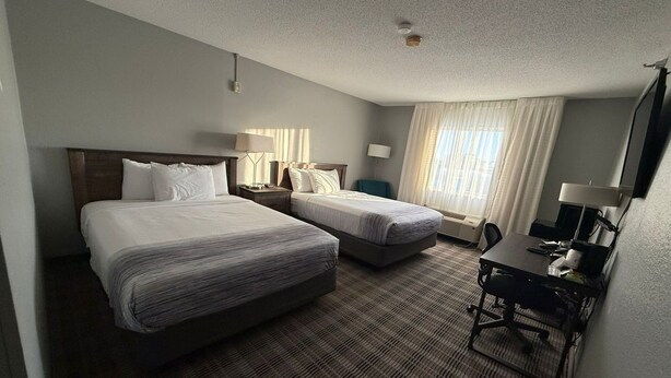 A hotel room with two beds, a desk, a chair, a TV, and a window with curtains.