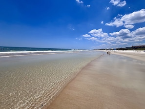 A wide sandy beach with clear water and a few people in the distance.