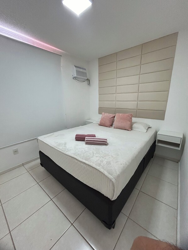 A bedroom with a bed, a bedside table, and a wall-mounted air conditioning unit.