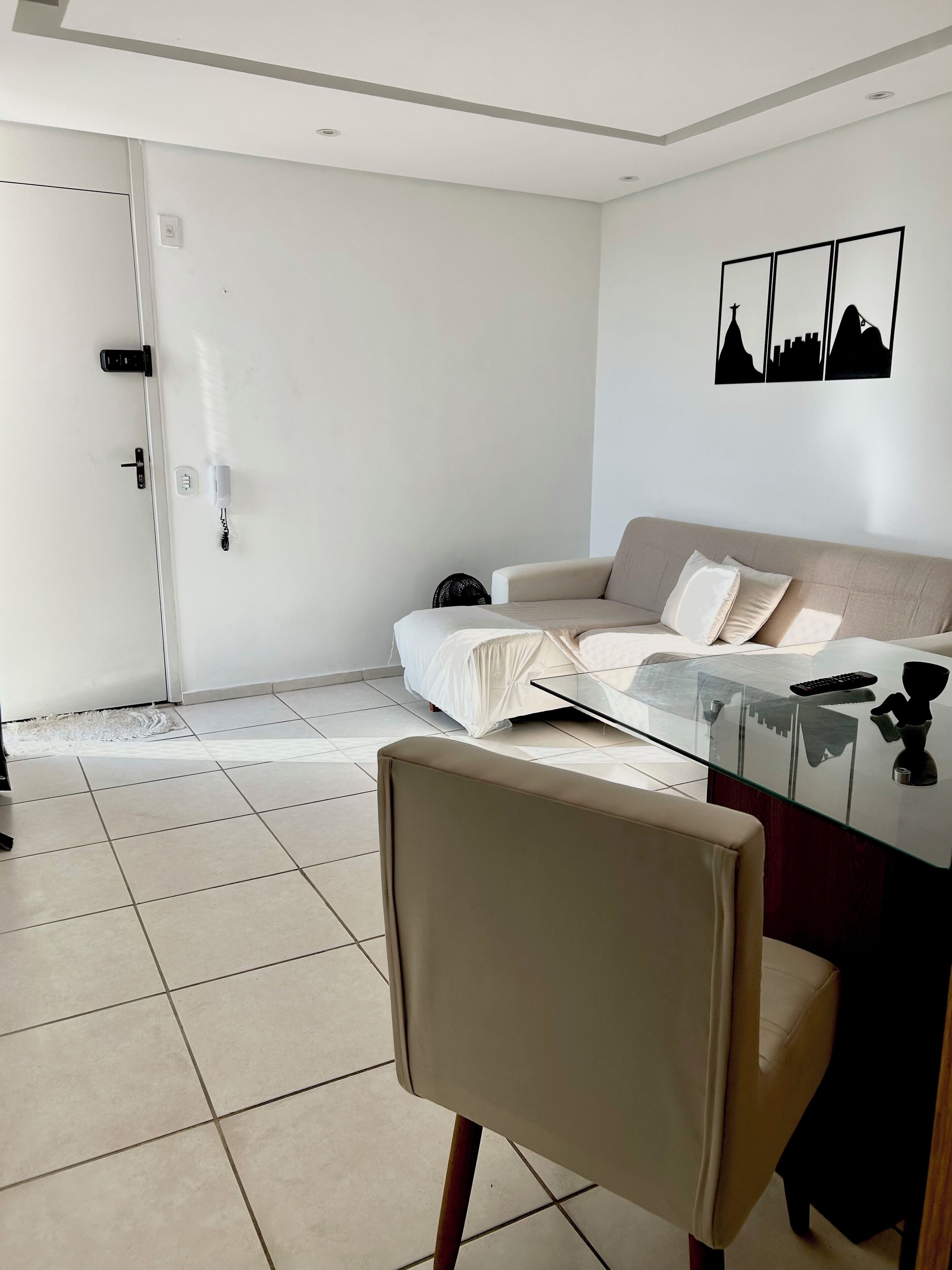 Een moderne woonkamer met een glazen salontafel, een beige bank en een witte deur.