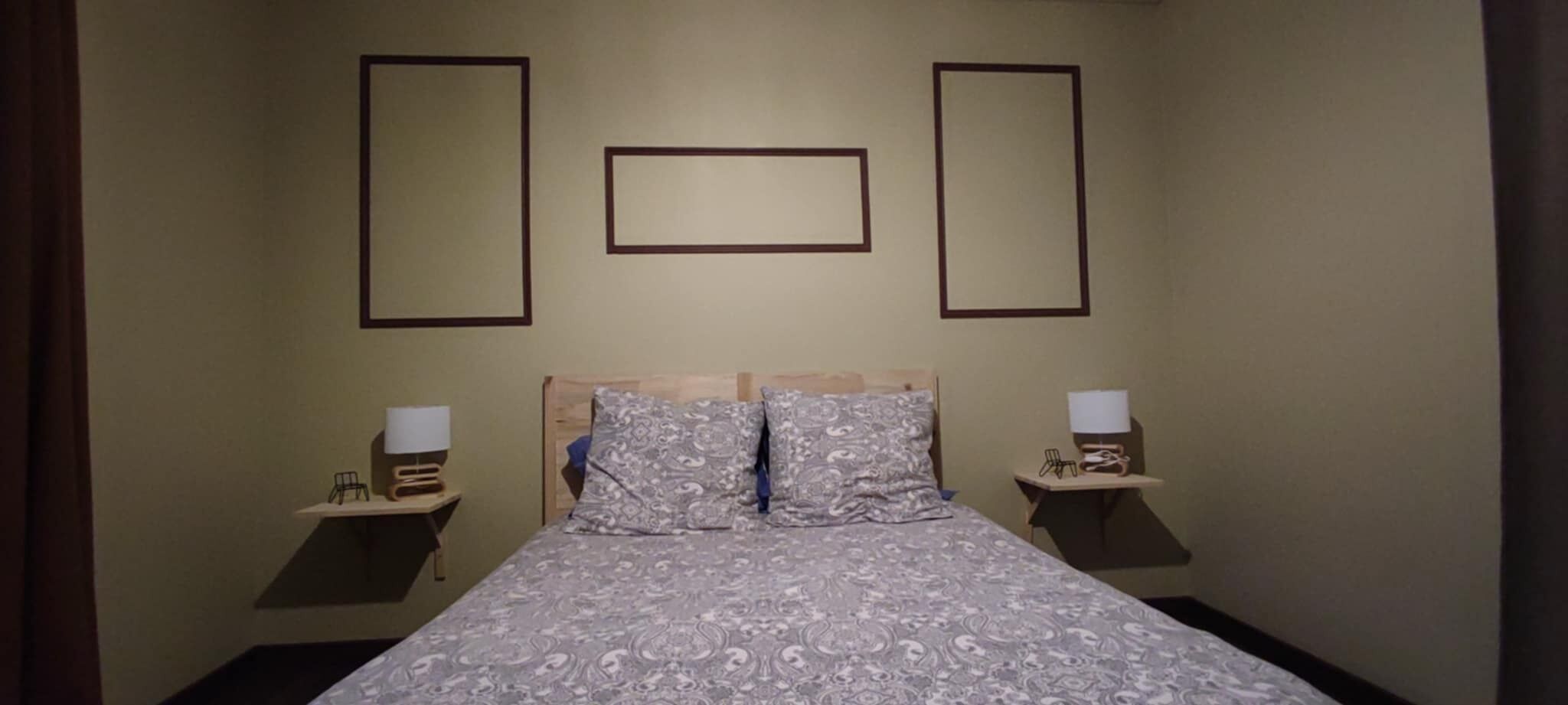 Une chambre d’hôtel comprenant un lit, deux tables de chevet et deux lampes fixées au mur.