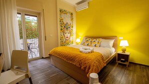 A bedroom with a large bed, a chair, a small table, a nightstand with a lamp, and a wall with a painting. - Terra d'Agrumi Rooms (Catania)