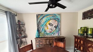 A dining area with a wooden table, chairs, a ceiling fan, a painting, and a decorative cabinet. - The Luxury Rustic Home, exceeding your expectations, not your budget! (Laredo)