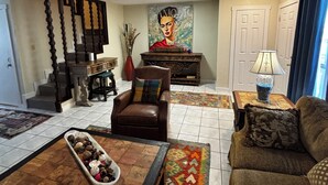 A living room with a brown leather sofa, a coffee table with decorative items, a brown armchair, a painting on the wall, and a ceiling fan. - The Luxury Rustic Home, exceeding your expectations, not your budget! (Laredo)