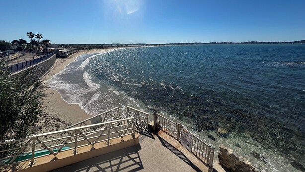 Une promenade en bord de mer offrant une vue dégagée sur l’océan, une plage de sable et une côte rocheuse.