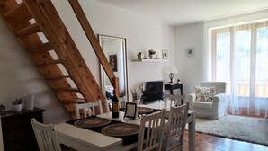 Un comedor con una mesa de madera, sillas blancas, un televisor y un sofá.
