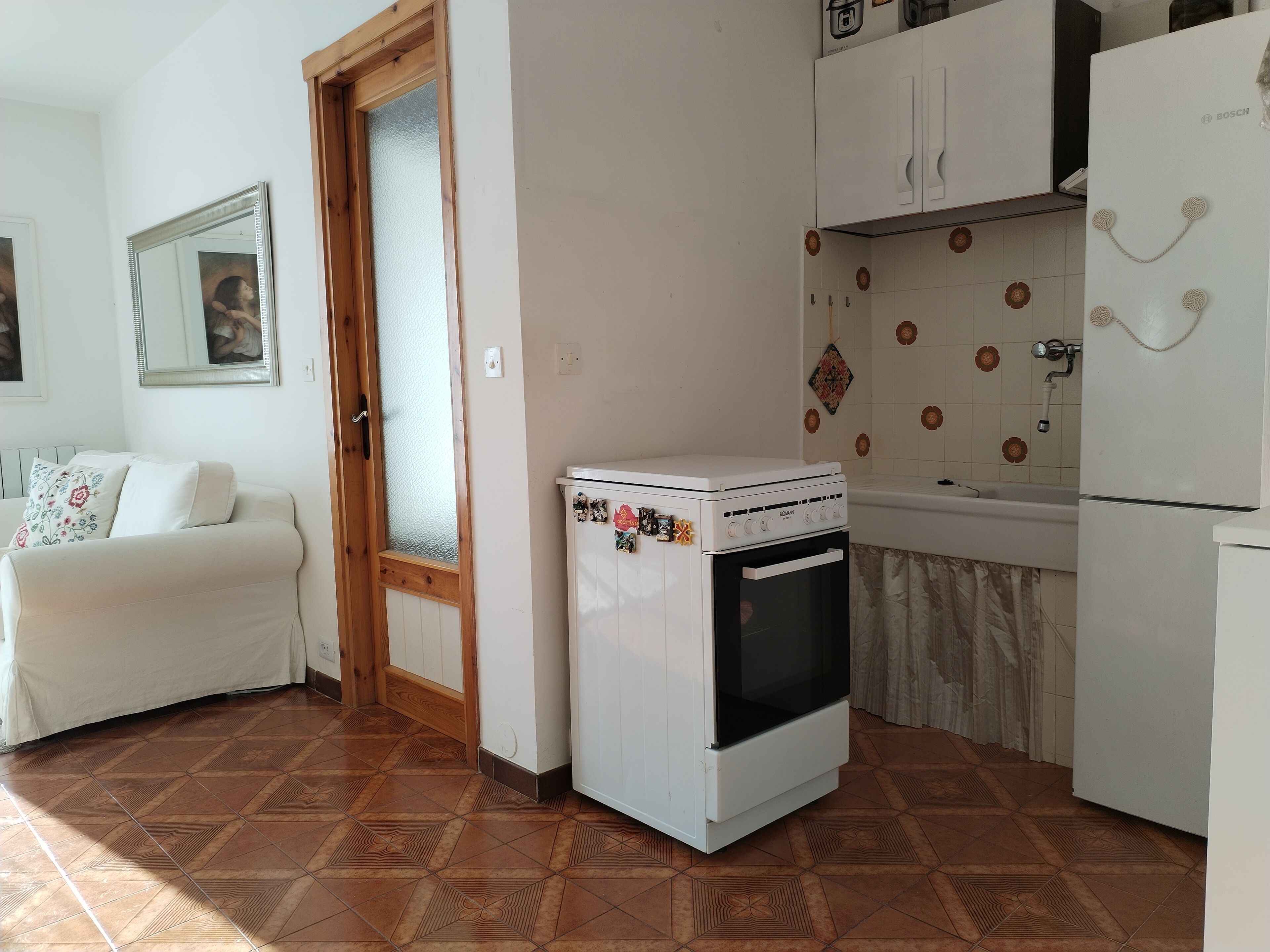 Una cocina compacta con horno blanco, un refrigerador y una zona de comedor con sofá blanco.