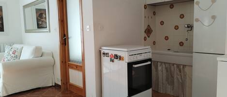 Una cocina compacta con horno blanco, un refrigerador y una zona de comedor con sofá blanco.