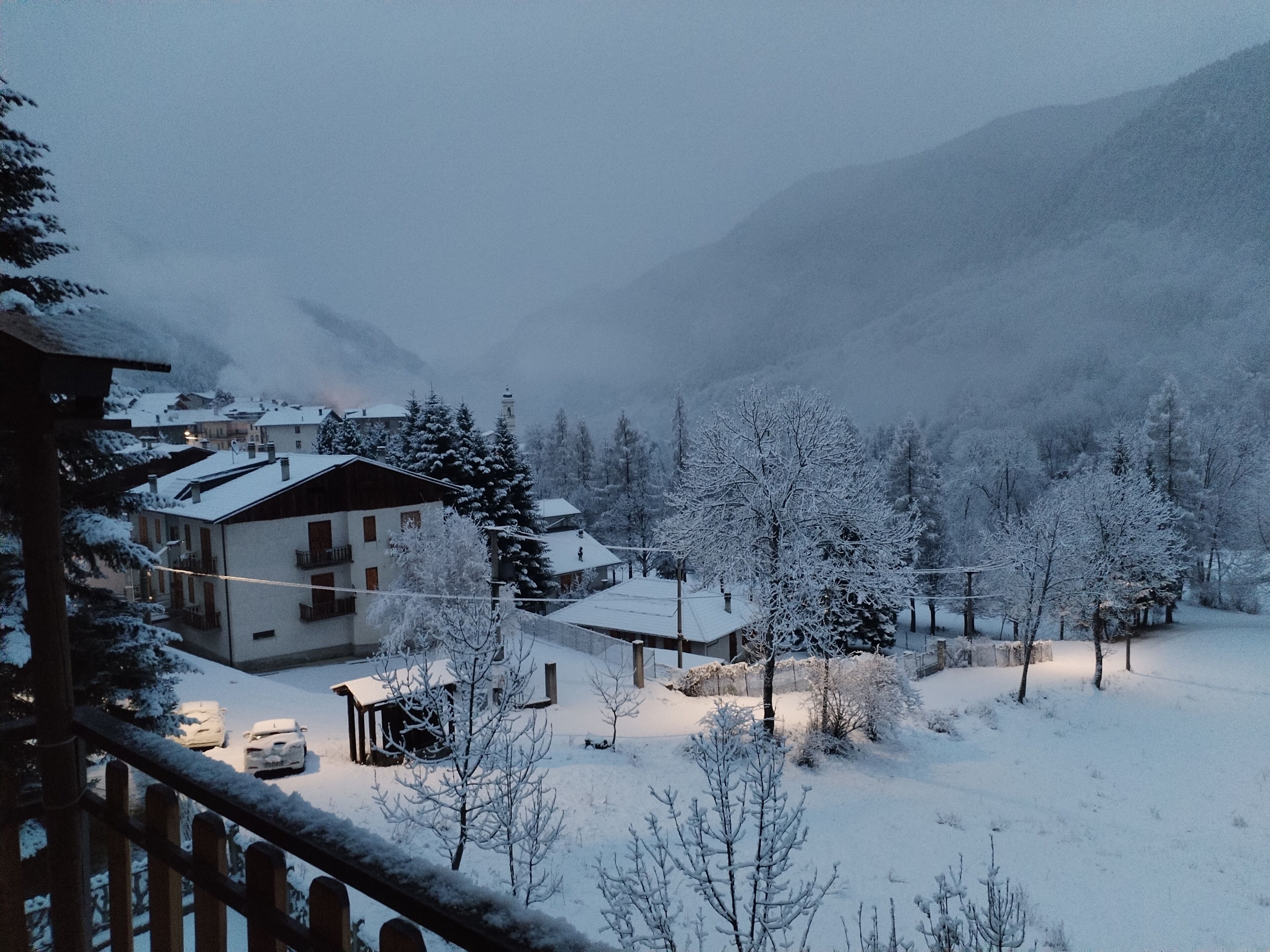 A snow-covered village with buildings and trees, surrounded by mountains.