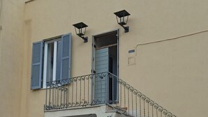 A building facade with a balcony, a door, and two wall-mounted lights. - Alice's House a stone's throw from the sea and the old town of Neptune (Nettuno)