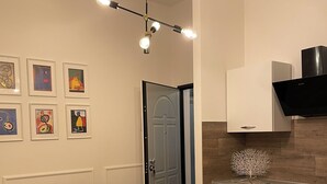 A modern living room with a gray sofa, a dining table with white chairs and yellow placemats, a kitchen with white cabinets and a black range hood, and a wall with framed artwork. - Alice's House a stone's throw from the sea and the old town of Neptune (Nettuno)