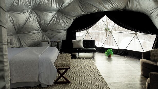 Um quarto de tenda acolhedor com uma cama, um banco, uma mesinha e um vaso com planta.