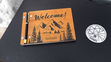 A wooden welcome sign with a mountain and tree design, labeled "Visitor Guest Book," and a circular sticker with "Sunny Side Domes" text.