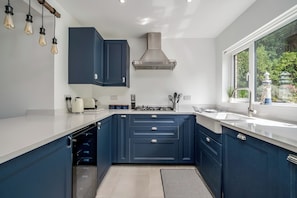 A modern kitchen with dark blue cabinets, a white countertop, and a stainless steel range hood.