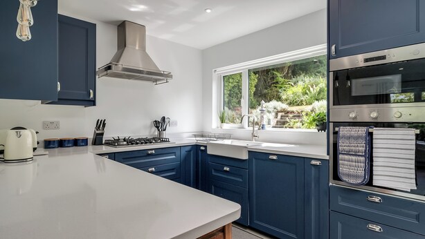 A modern kitchen with blue cabinets, a stainless steel range hood, and a large window providing a view of greenery outside. - Stunning home over looking Belfast City, 11 minutes to City Centre (Castlereagh)