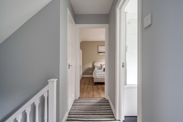 A hallway with a striped carpet leading to a bedroom with a bed and an air conditioner.