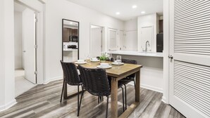 A modern kitchen with white cabinets, a wooden dining table set for four, and a large mirror above the counter. - DC Charm in Crystal Apartments (Arlington)