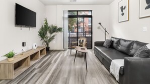 A modern living room with a flat-screen TV, a wooden bench, a black leather sofa, and a large window with a view of buildings. - DC Charm in Crystal Apartments (Arlington)