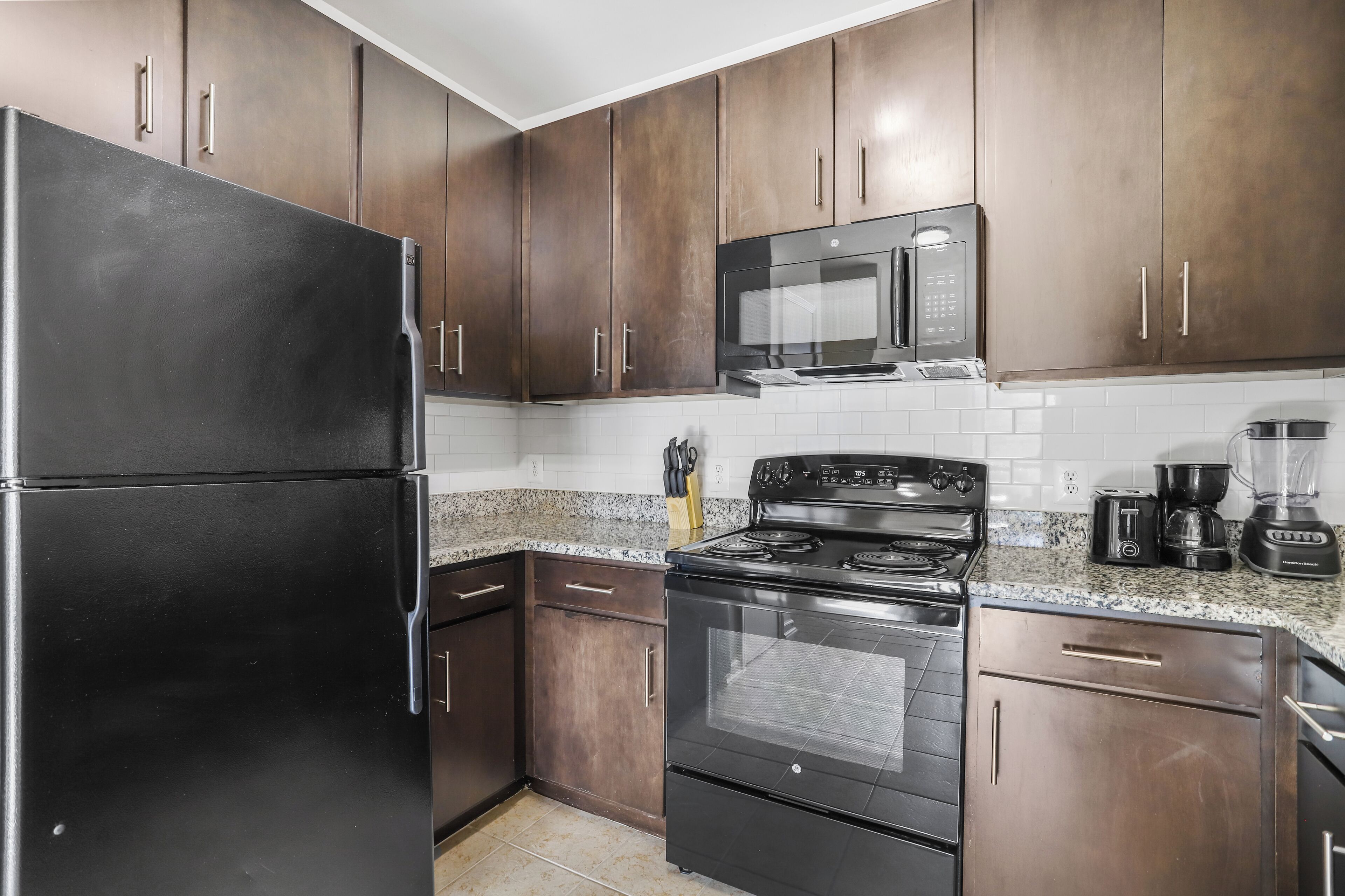 A kitchen with dark wooden cabinets, a black refrigerator, a microwave, a stove, and a coffee maker.