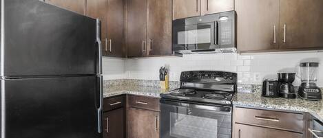 A kitchen with dark wooden cabinets, a black refrigerator, a microwave, a stove, and a coffee maker.