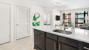 A modern kitchen with a dishwasher, a sink, and a countertop. There is a mirror above the sink and a television mounted on the wall. - DC Charm in Crystal Apartments (Arlington)