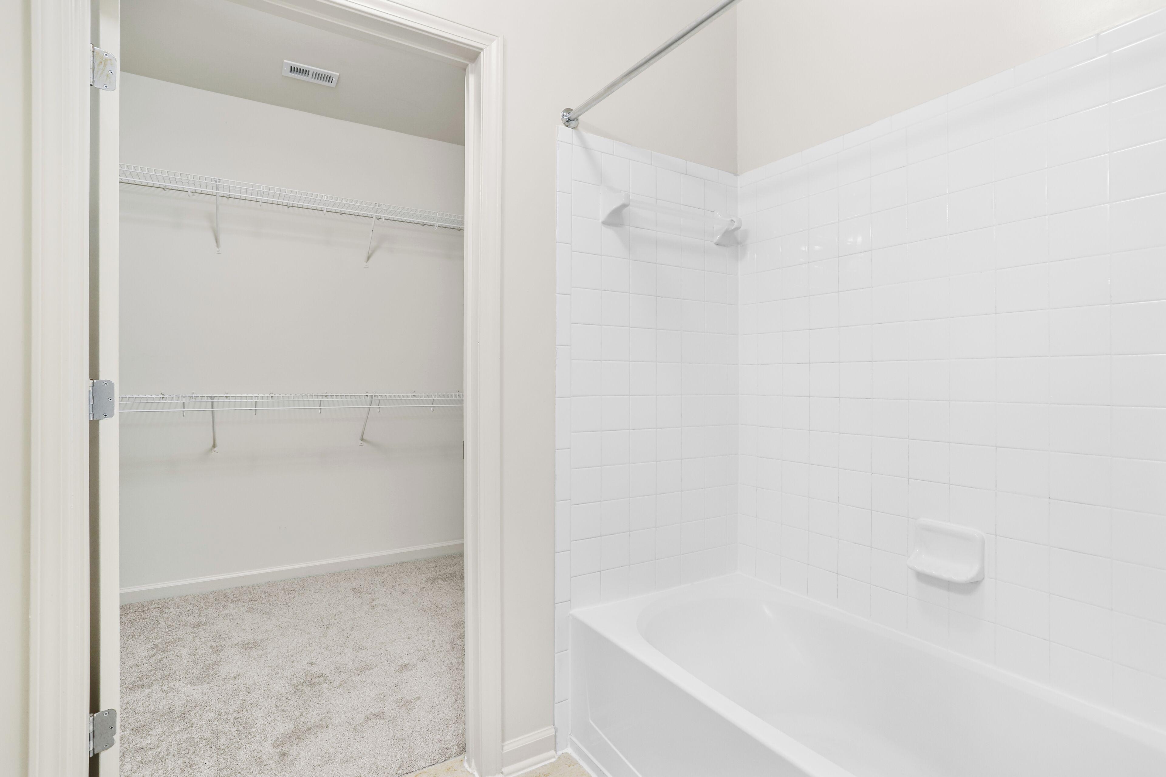A bathroom with white tiled walls, a bathtub, and a walk-in closet with shelves.